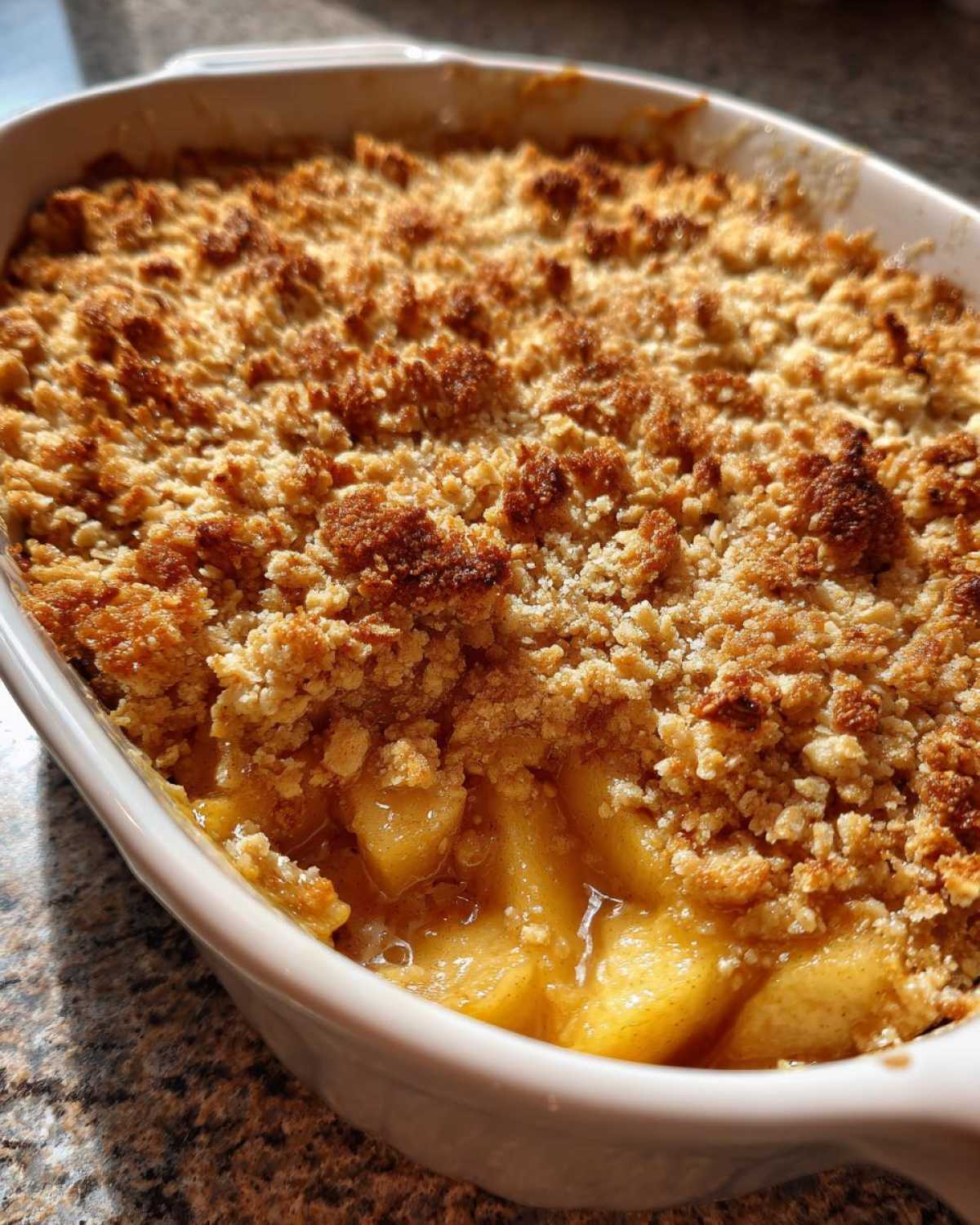 Close-up view of a baked apple crumble in a white dish, showing the golden brown crumb topping and bubbling apple filling.