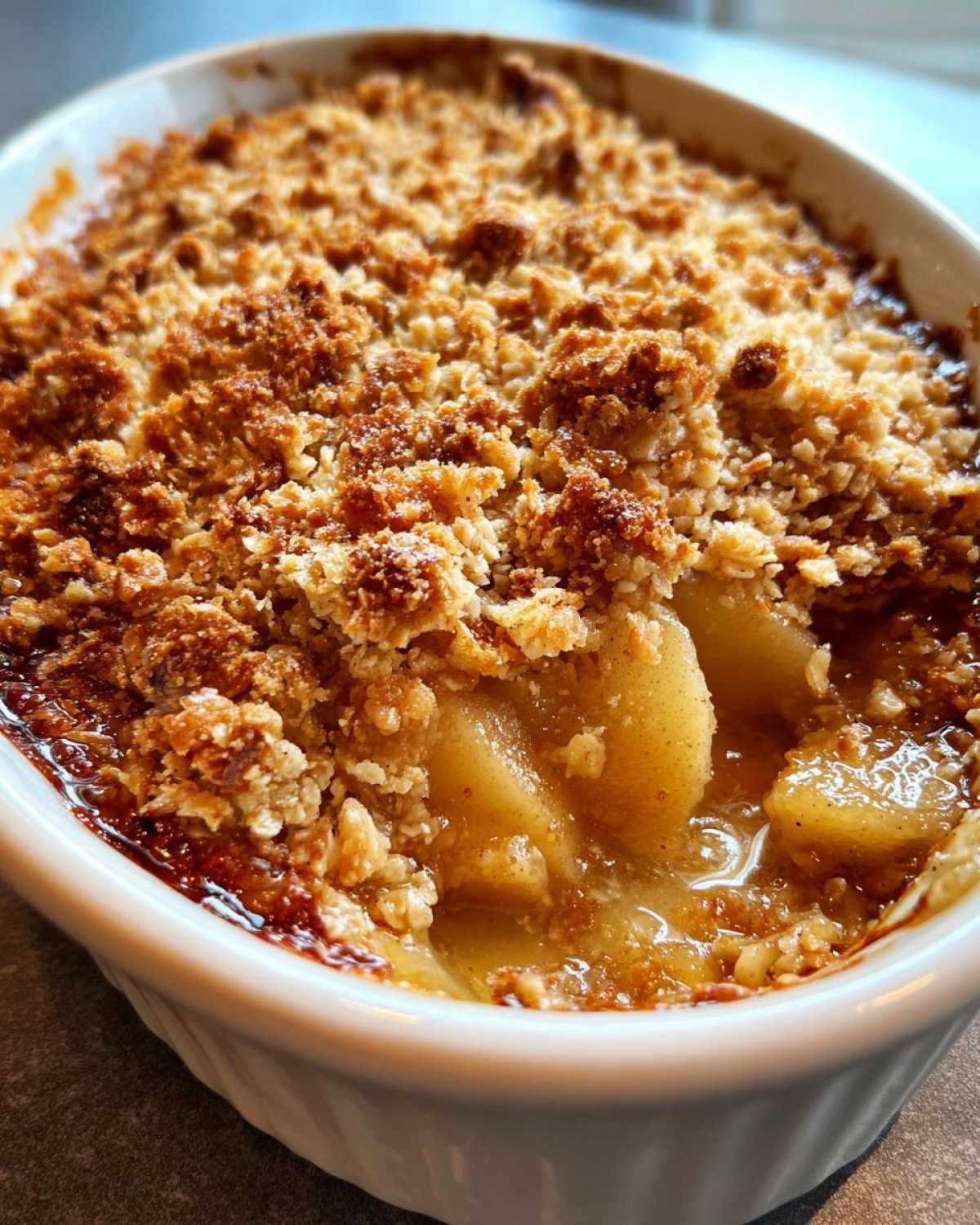 Close-up of a warm apple crumble in a white dish, showing the golden brown topping and bubbling apple filling.