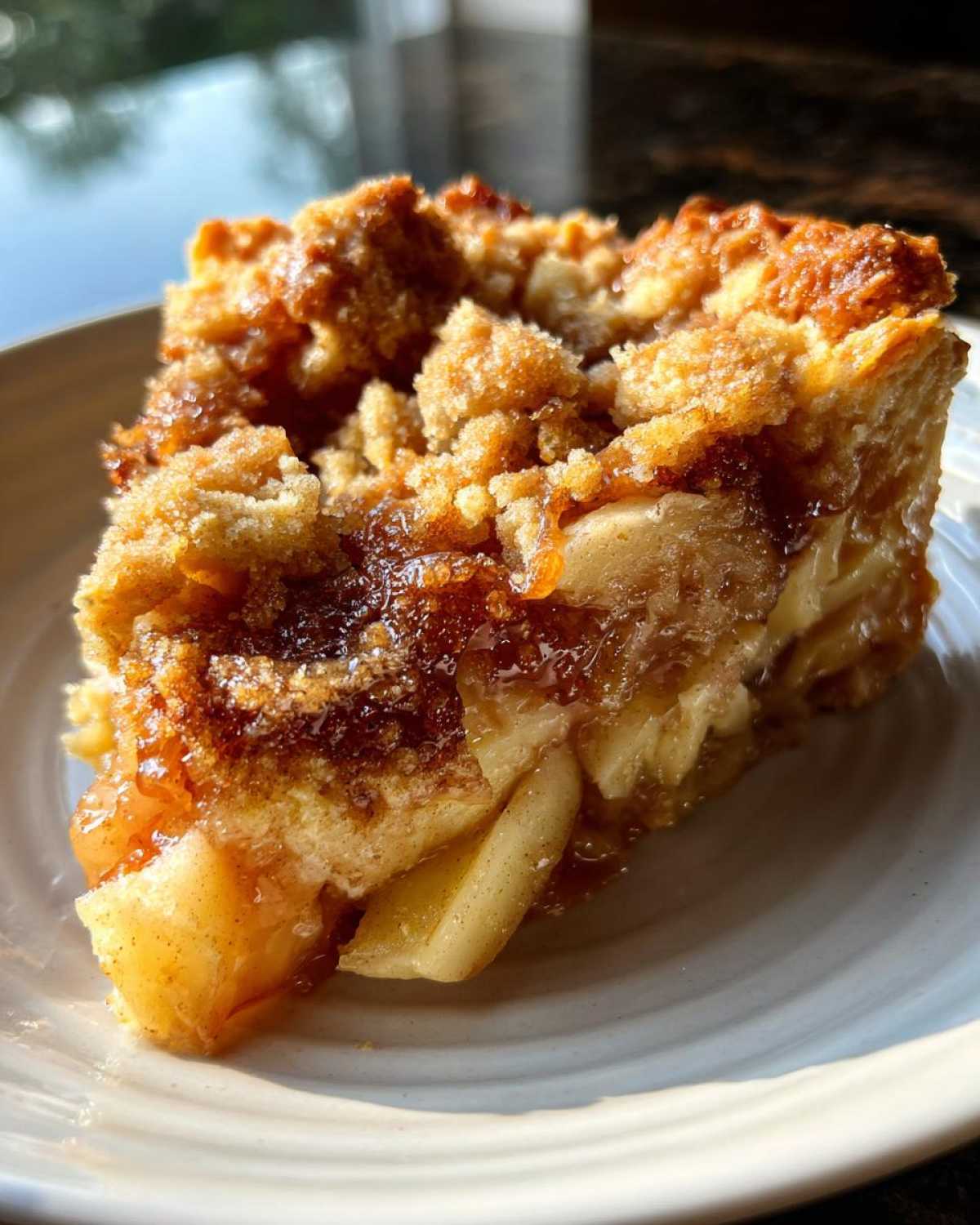 Close-up of a slice of apple pie dump cake on a white plate, showing the crumb topping and apple filling.