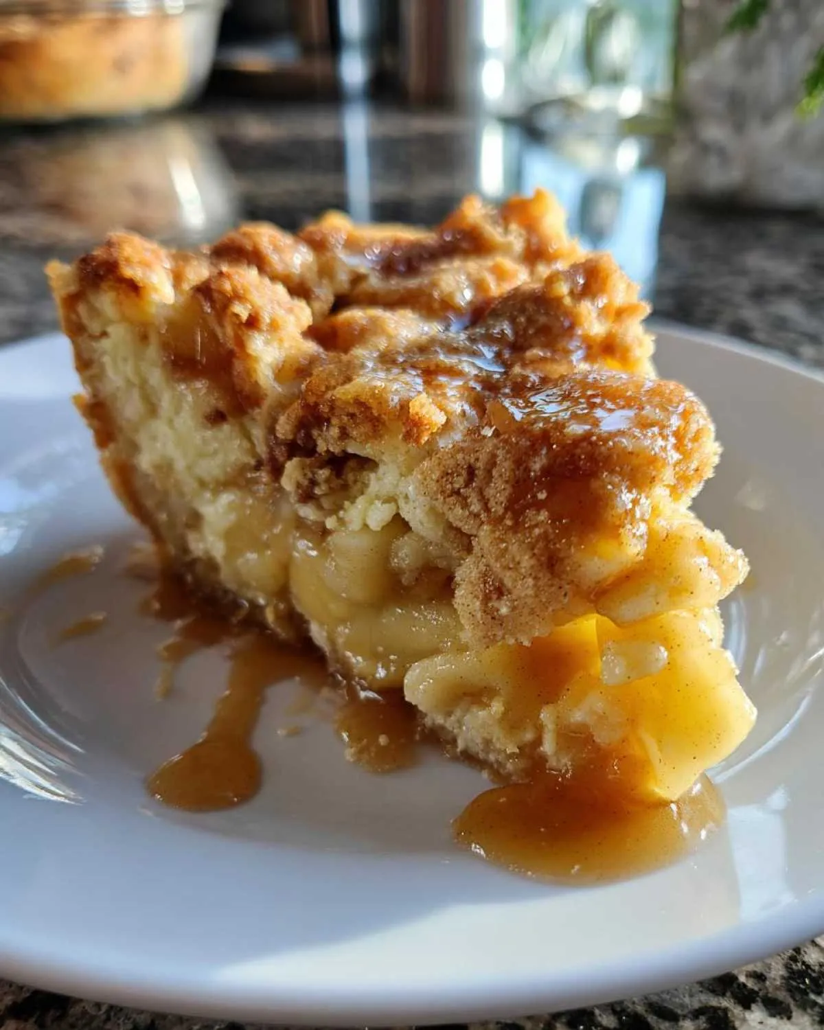 Close-up of a slice of apple pie dump cake on a white plate, with caramel sauce drizzled over the top.