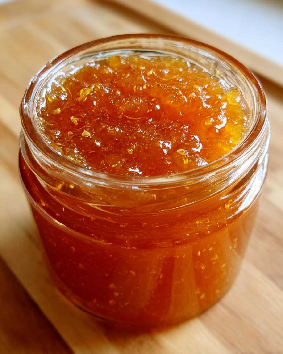 Close-up of a glass jar filled with bright orange apricot jam on a wooden surface.