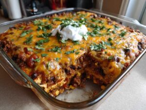 A close-up view of a baked mexican casserole in a glass dish, topped with melted cheese, fresh cilantro, and a dollop of sour cream.