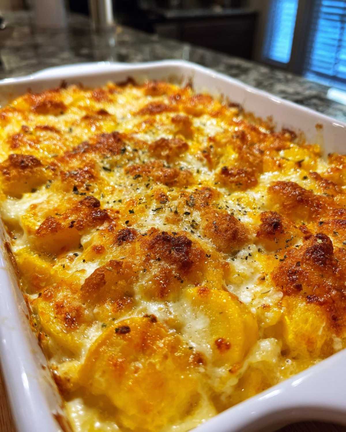 Close-up of a baked squash casserole in a white dish with a bubbly, golden cheese and breadcrumb topping.