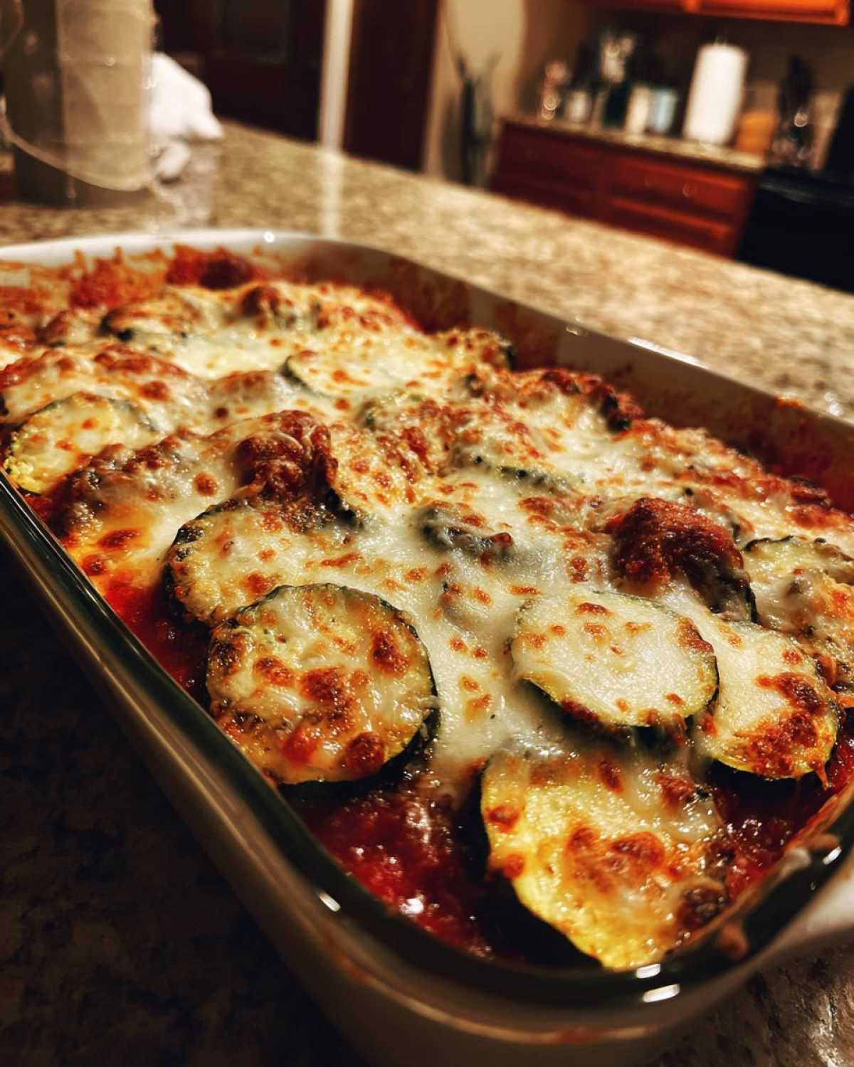 A close-up of a baking dish filled with golden-brown, bubbly zucchini parmesan, showing melted cheese and tomato sauce.