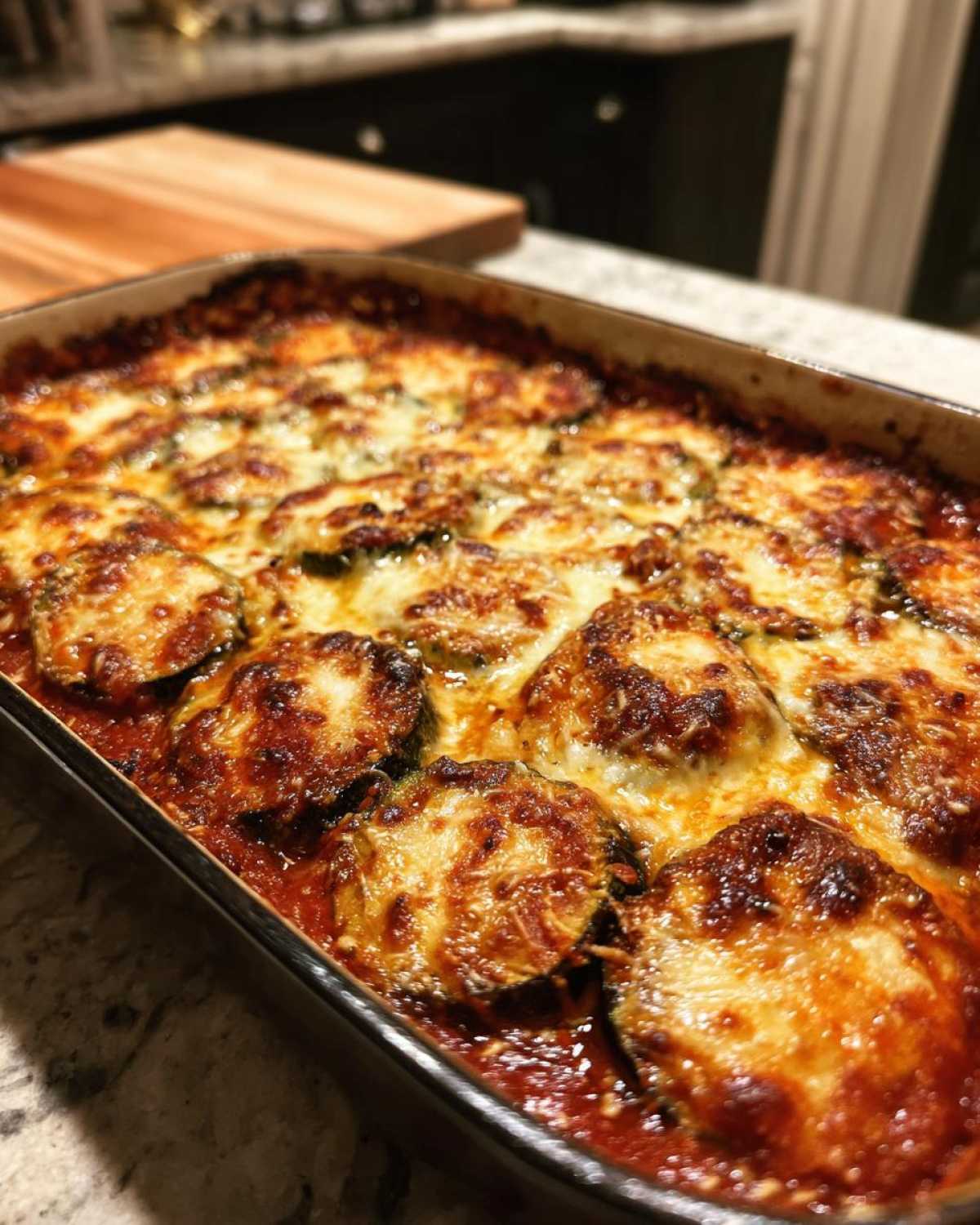 A close-up of a baking dish filled with golden-brown, bubbly zucchini parmesan, fresh out of the oven.