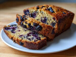 A golden-brown loaf of blueberry zucchini bread with two slices cut, showing the moist interior and visible blueberries.