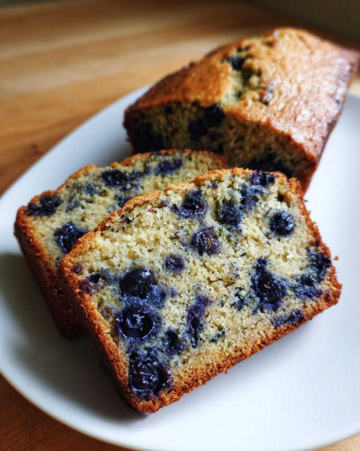 Close-up of a loaf of blueberry zucchini bread with two slices cut and placed in front on a white plate.