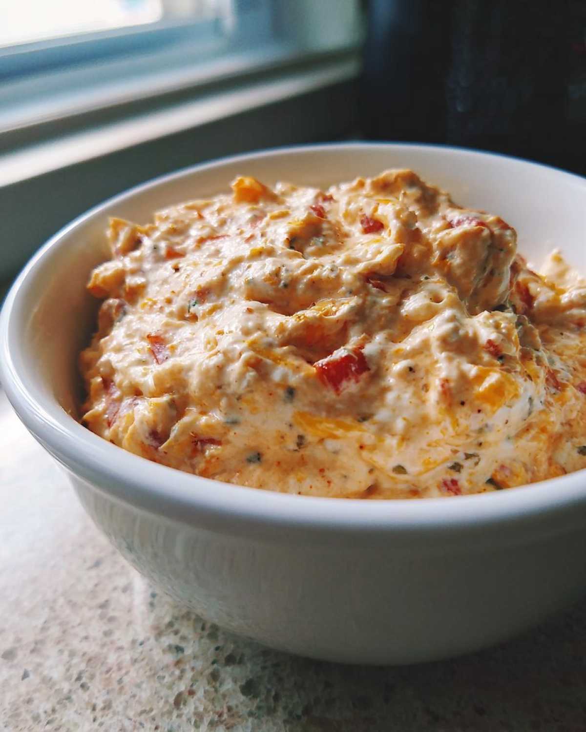 A close-up shot of a white bowl filled with creamy Boat dip rotel ranch dip, showing red and orange specks.
