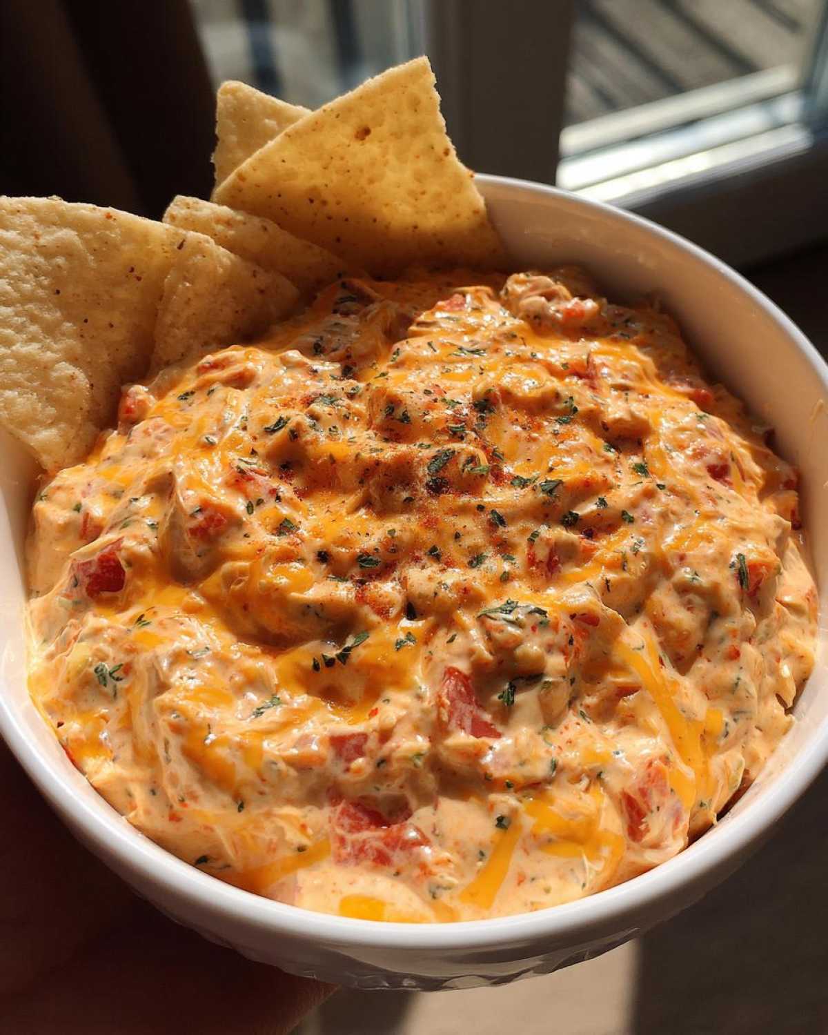 Close-up of a white bowl filled with creamy Boat dip, topped with melted cheese, herbs, and served with tortilla chips.