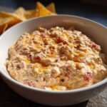 A white bowl filled with creamy Boat dip, topped with melted cheese and black pepper, with tortilla chips in the background.