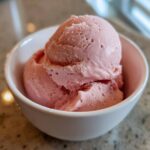 Two scoops of pink cottage cheese ice cream in a white bowl on a speckled countertop.