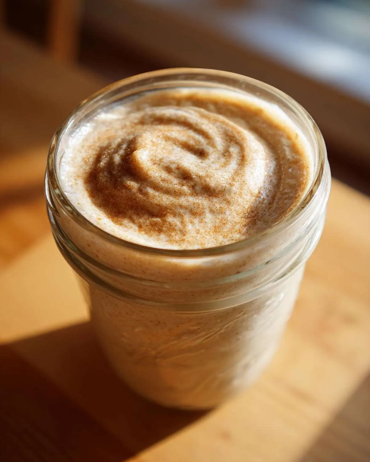 Close-up of creamy blended overnight oats in a glass mason jar, topped with a swirl and a sprinkle of cinnamon.