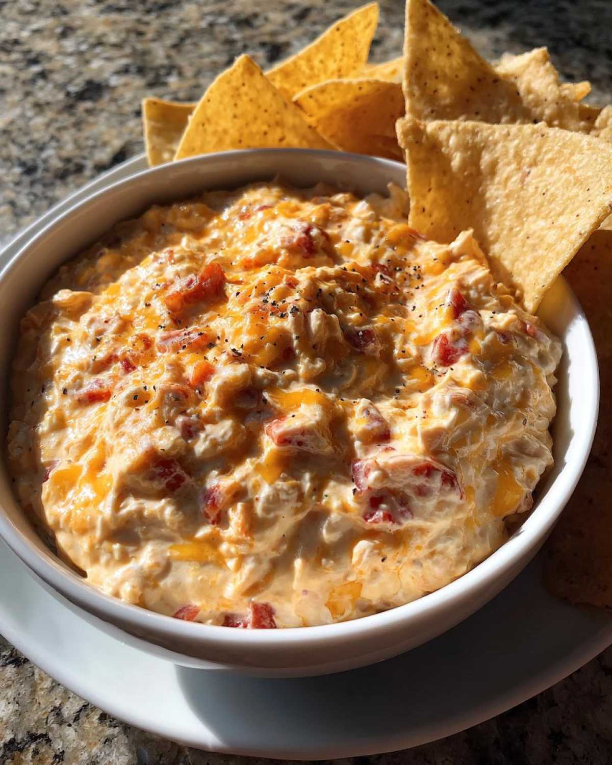 A white bowl filled with creamy Boat dip, topped with red bell peppers and black pepper, surrounded by tortilla chips.