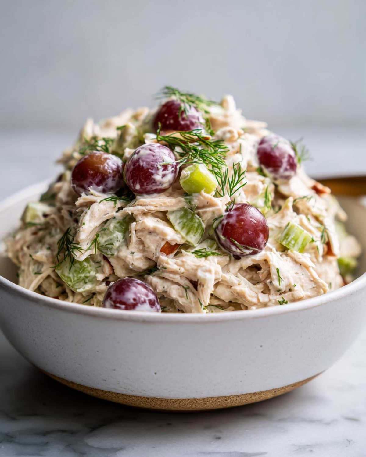 Close-up of a bowl of creamy chicken salad recipe with red grapes, celery, and fresh dill on top.