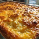 Close-up of a creamy squash casserole in a glass baking dish with a golden brown, bubbly top.