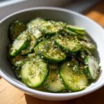 Close-up of a bowl of fresh cucumber salad with sliced cucumbers, dill, and sesame seeds.
