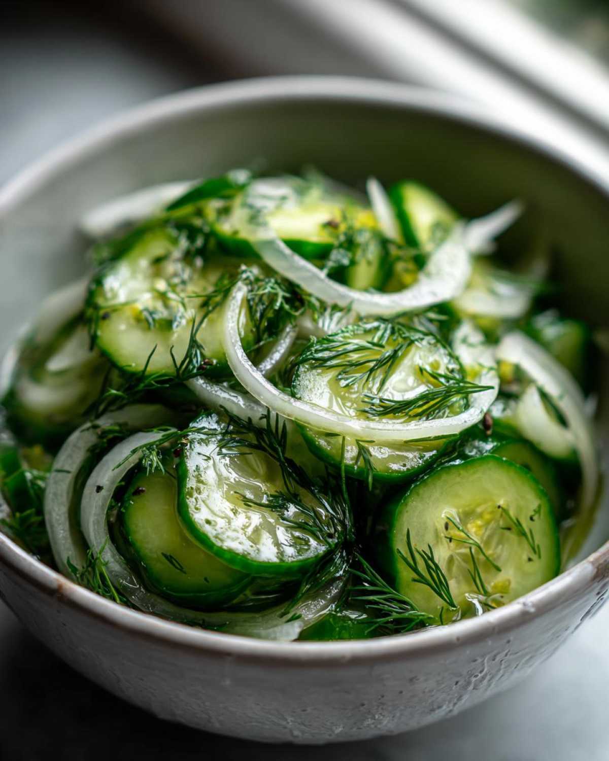 Close-up of a bowl of sliced cucumbers and onions in vinegar, garnished with fresh dill.