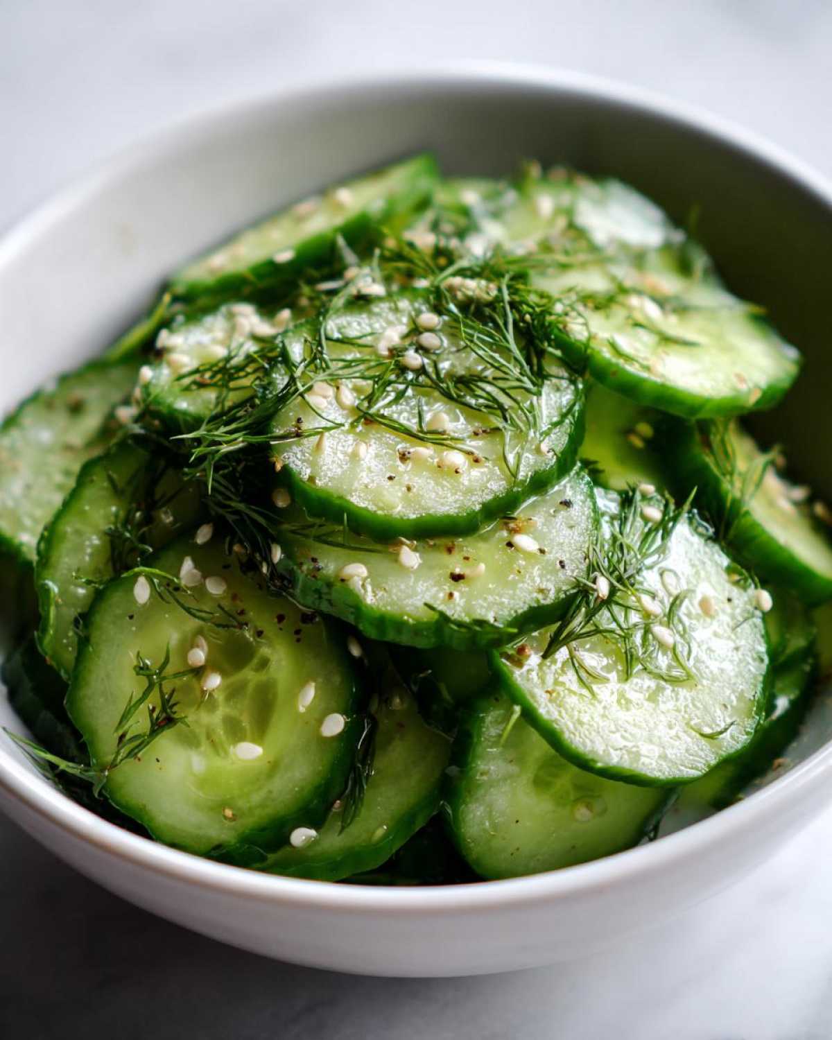 Close-up of a bowl of crisp cucumber salad with fresh dill, sesame seeds, and black pepper.