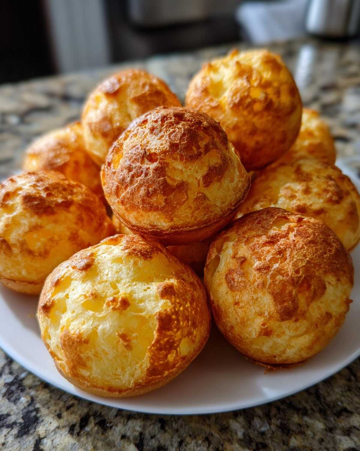 A close-up shot of a pile of golden-brown, freshly baked Brazilian cheese bread on a white plate.