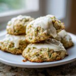 A stack of zucchini cookies on a white plate, topped with a creamy white glaze.