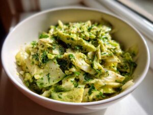 Close-up of a vibrant green goddess salad in a white bowl, featuring chopped cabbage, cucumbers, and a creamy green dressing.