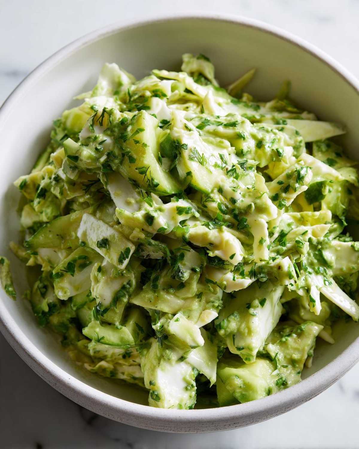 Close-up shot of a white bowl filled with green goddess salad, showing chopped vegetables and creamy green dressing.