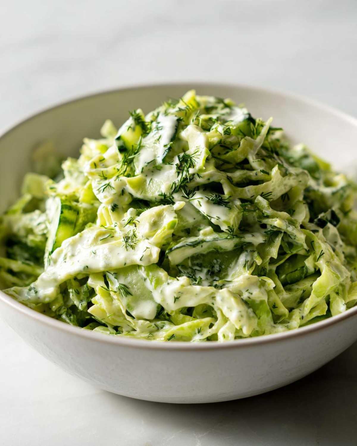 Close-up shot of a white bowl filled with green goddess salad, showing shredded cabbage, cucumber, and creamy dressing.