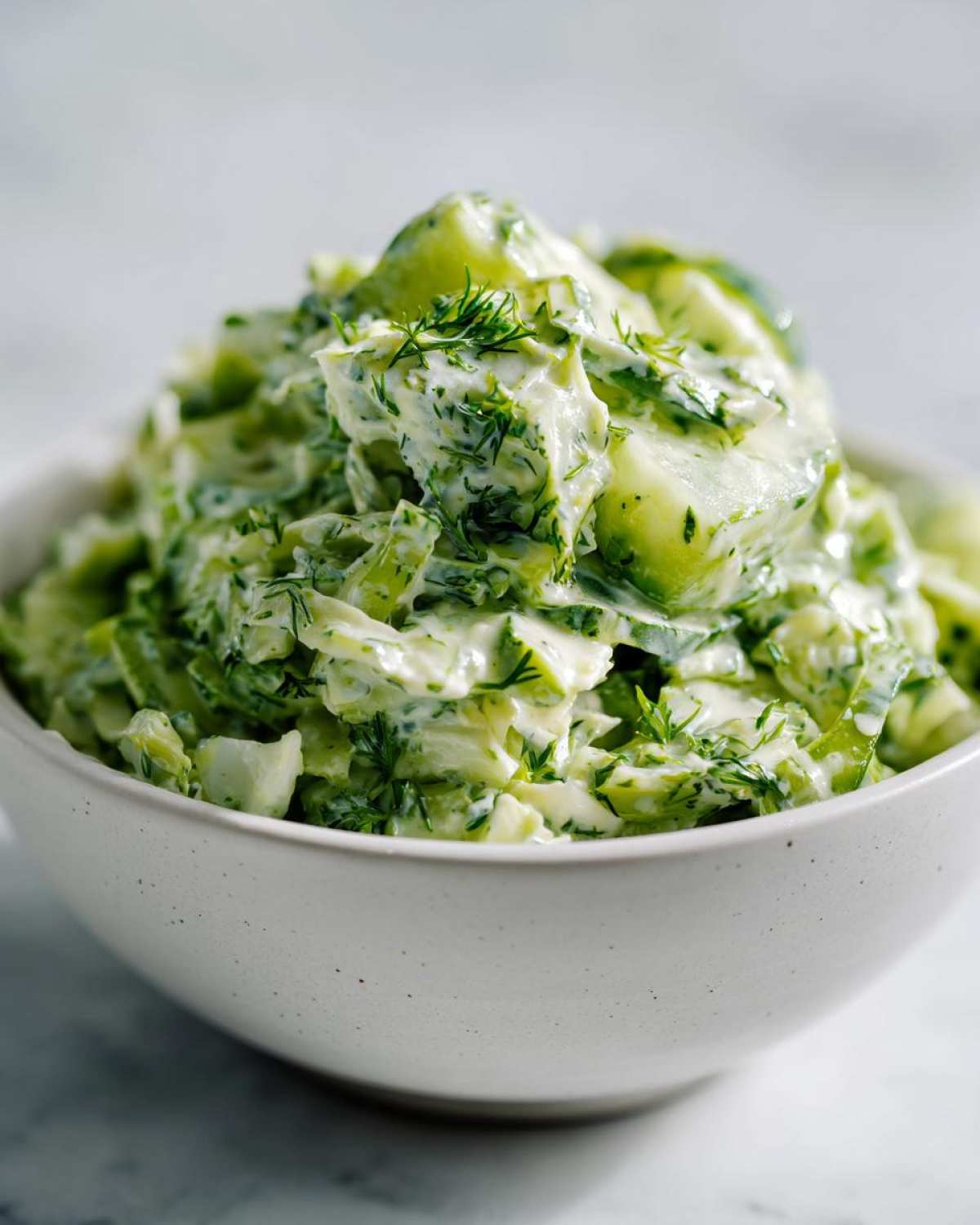 Close-up of a bowl filled with green goddess salad, showing chopped cucumbers and herbs coated in a creamy green dressing.