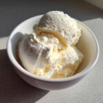 Three scoops of creamy high protein cottage cheese ice cream in a white bowl, lit by sunlight.