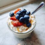 Close-up of high protein overnight oats in a glass jar, topped with fresh blueberries, sliced strawberries, and a drizzle of honey.