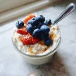 Close-up of high protein overnight oats in a glass jar, topped with fresh blueberries, sliced strawberries, and a drizzle of honey.