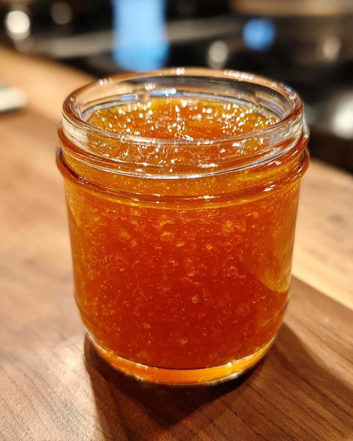 Close-up of a small glass jar filled with bright orange apricot jam on a wooden surface.