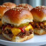 Close-up of several homemade cheeseburger sliders on a white plate, with melted cheese, pickles, and ketchup.