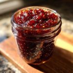 A close-up shot of a clear glass jar filled with rich, dark red fig jam, showing the texture and fig seeds.