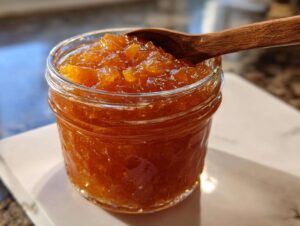 Close-up of a glass jar filled with homemade peach jam, with a wooden spoon resting on top.