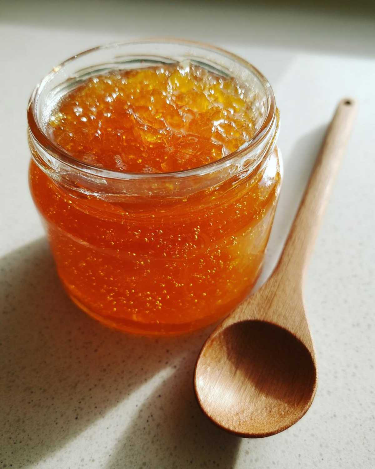 A glass jar filled with bright orange peach jam next to a small wooden spoon.