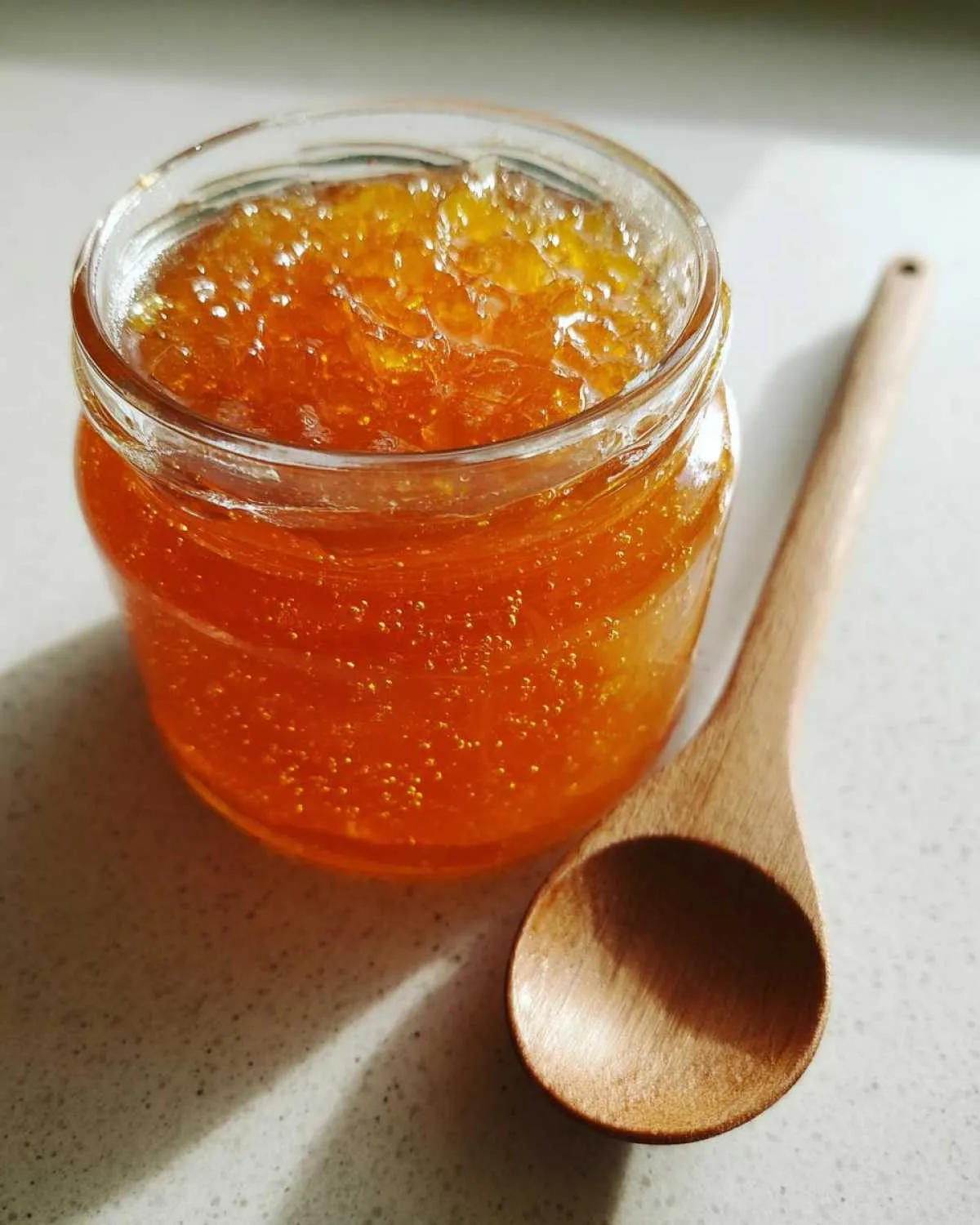 A glass jar filled with bright orange peach jam next to a small wooden spoon.