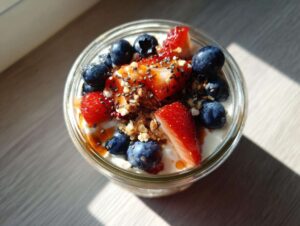 Close-up of a glass jar filled with overnight oats, topped with fresh strawberries, blueberries, chia seeds, and a drizzle of syrup.