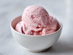 A close-up of a white bowl filled with scoops of pink cottage cheese ice cream, showing a smooth, creamy texture.