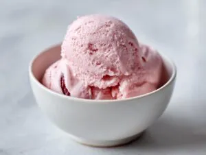 A close-up of a white bowl filled with scoops of pink cottage cheese ice cream, showing a smooth, creamy texture.