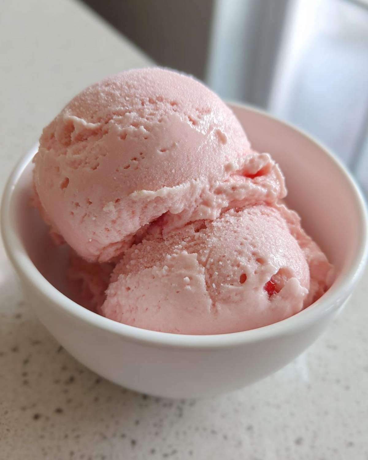 Close-up of two scoops of light pink cottage cheese ice cream in a white bowl, showing a smooth, creamy texture.