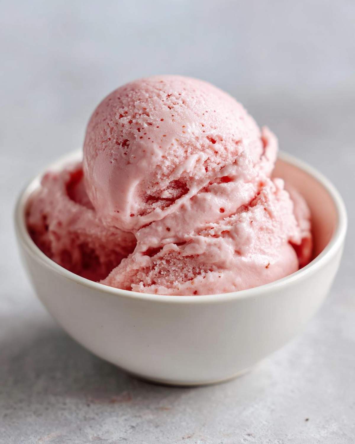 Close-up of two scoops of pink cottage cheese ice cream in a white bowl.