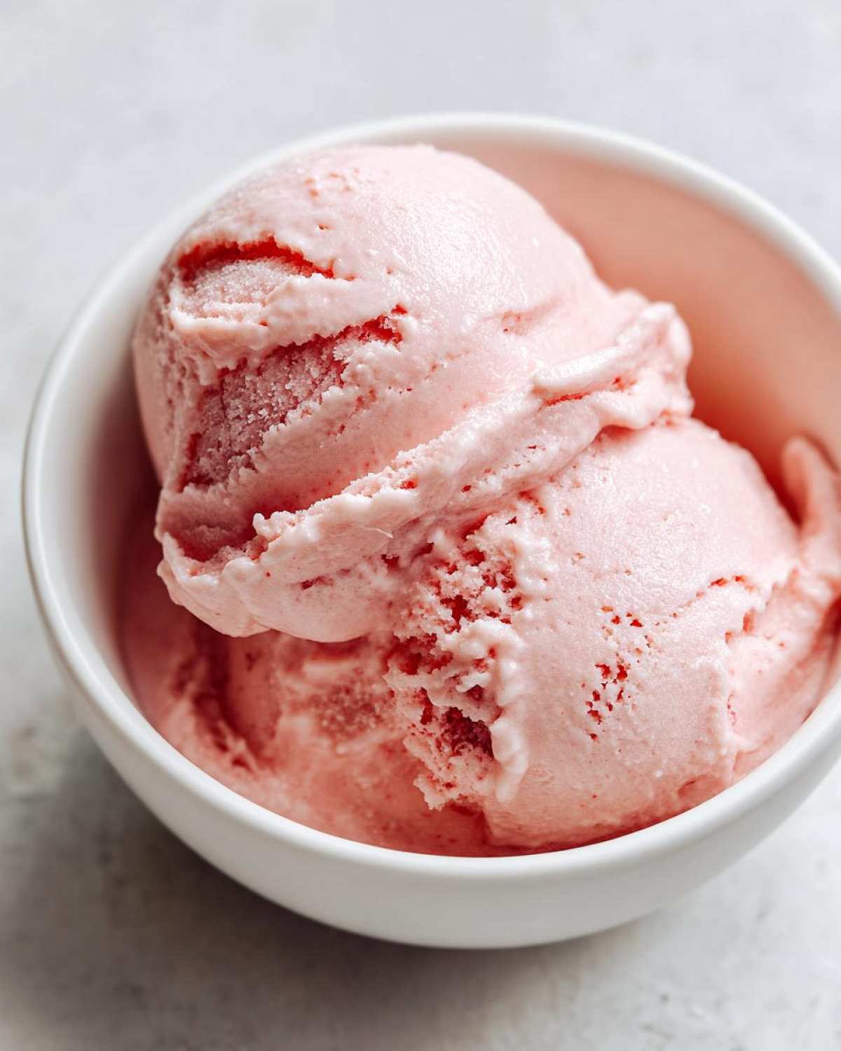 Two scoops of light pink cottage cheese ice cream in a white bowl, showing a smooth, creamy texture.