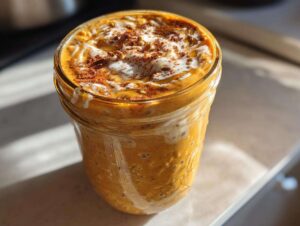 Close-up of creamy pumpkin overnight oats in a glass jar, topped with yogurt, cinnamon, and seeds.