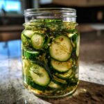 A clear glass jar filled with sliced cucumbers, fresh dill, and pickling spices, ready to become refrigerator pickles.