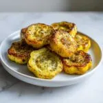 A white plate filled with golden-brown, roasted patty pan squash, seasoned with herbs and garlic.