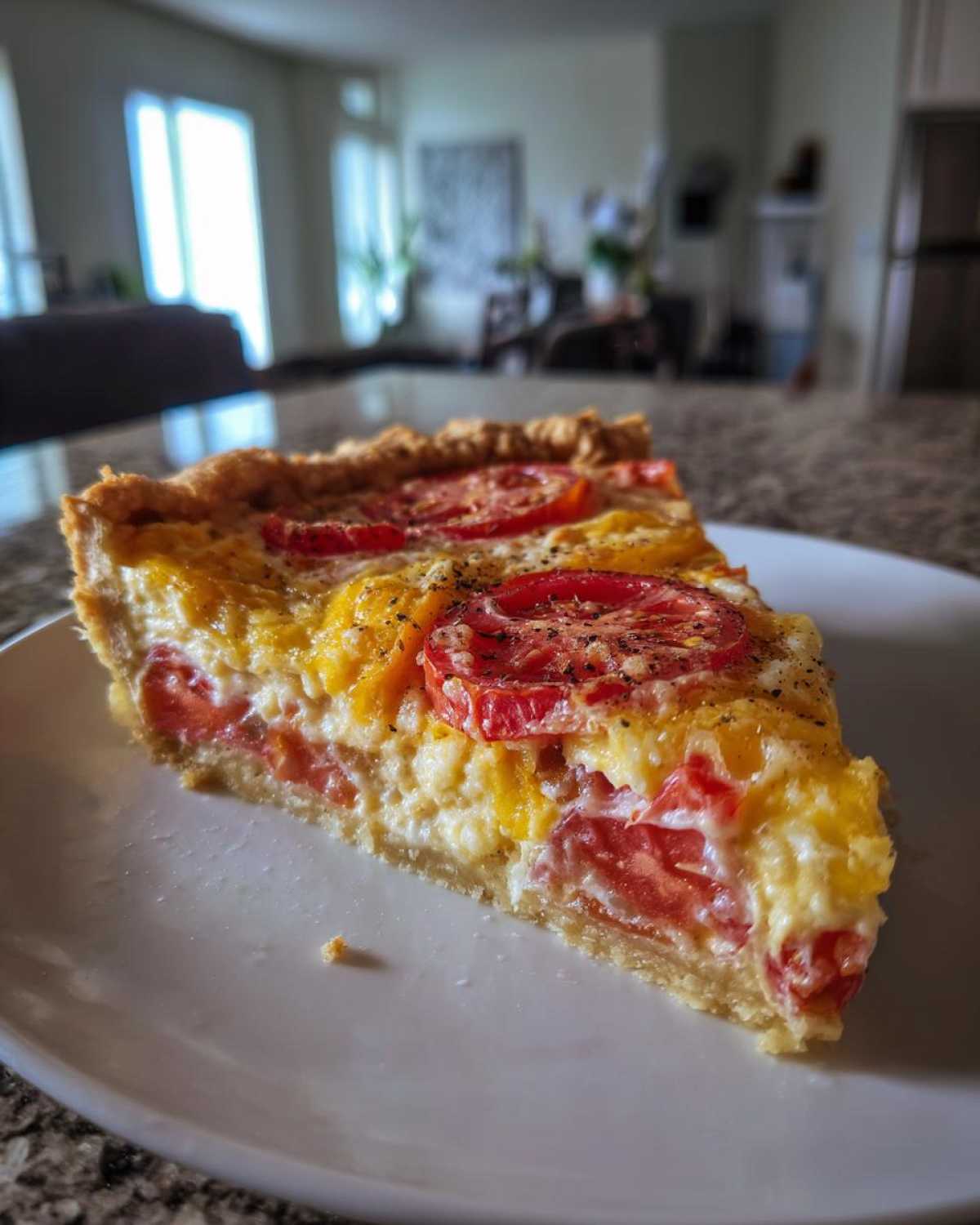 Close-up of a slice of tomato pie on a white plate, showing layers of red and yellow tomatoes, creamy filling, and a flaky crust.