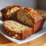 Close-up of a golden-brown loaf of Starbucks banana bread with a slice cut, showing moist texture and walnuts.