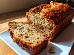 A golden brown loaf of Starbucks banana bread with a slice cut, revealing walnuts and moist texture.