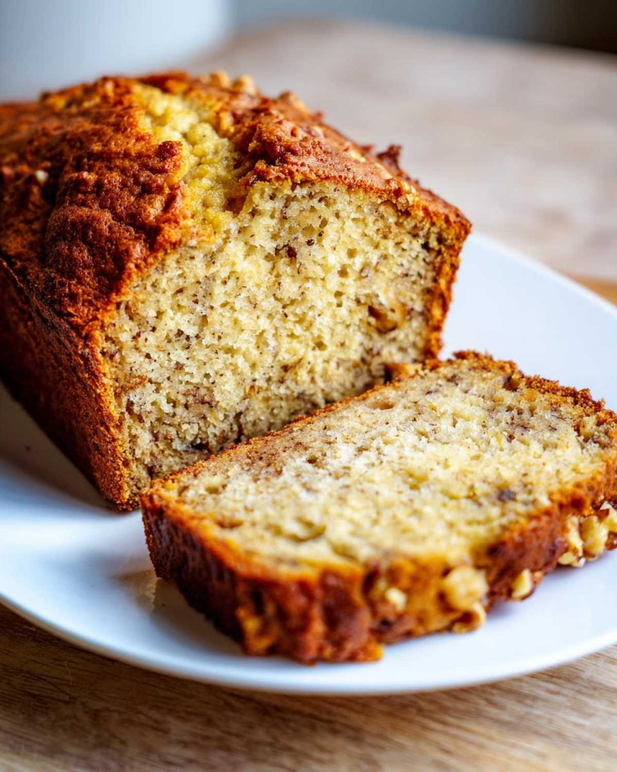A whole loaf of Starbucks banana bread with one slice cut and resting on a white plate, showing the moist texture and walnuts.